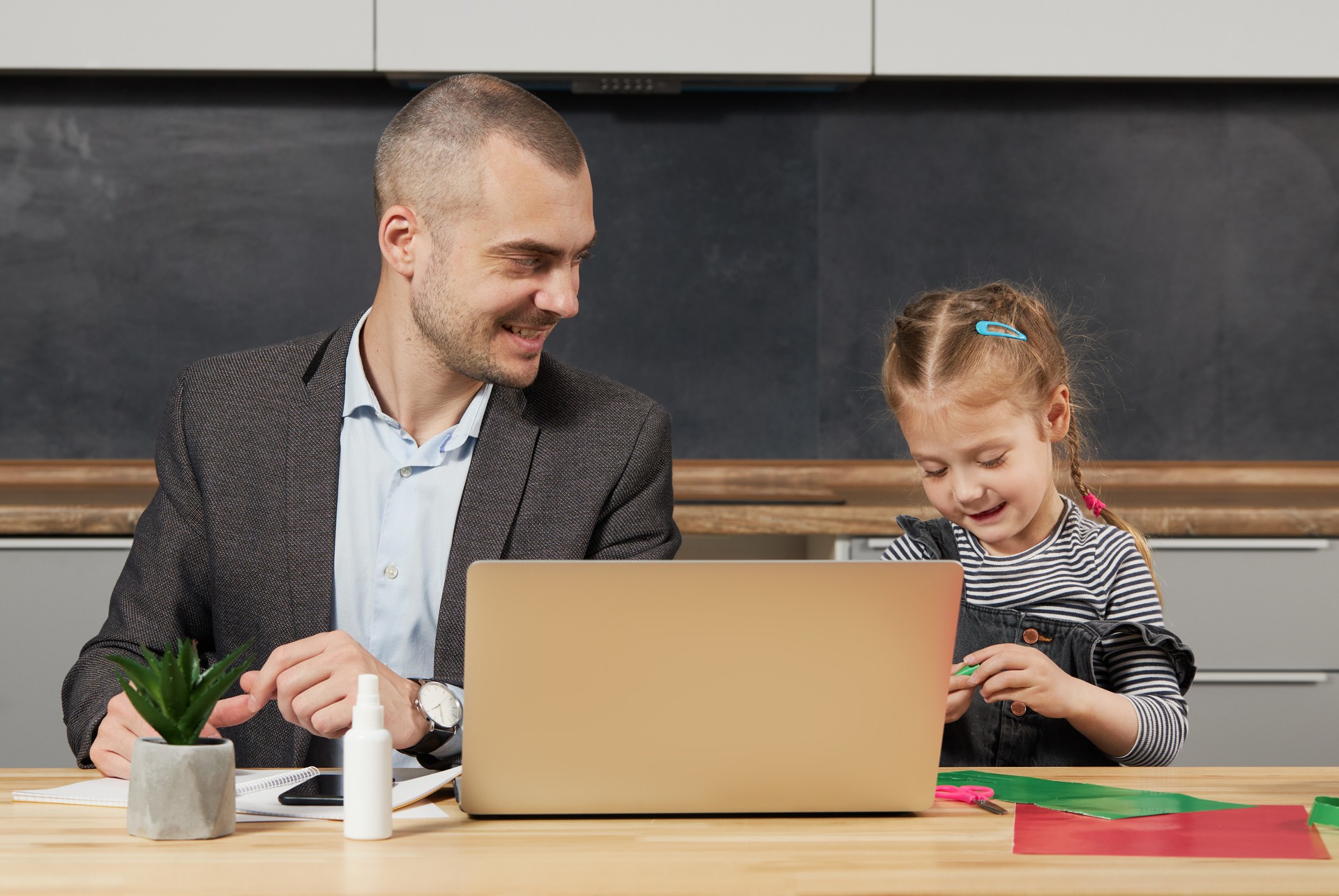 Father Working from home on laptop during quarantine. Little child girl make noise and distracts father from work on the kitchen office