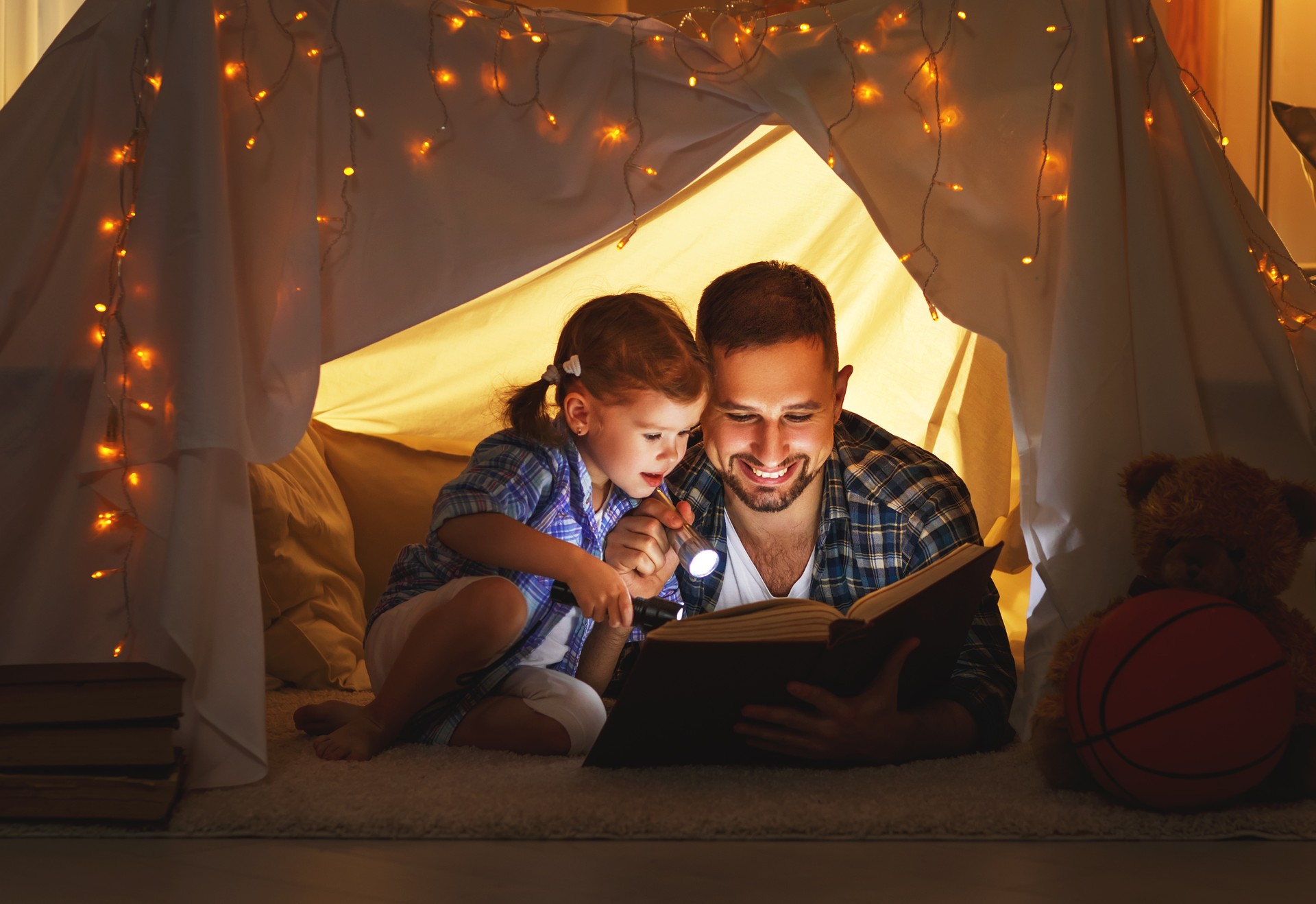 happy family father and child daughter reading a book  in  tent at home